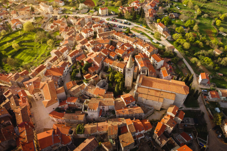 Aerial view of a compact historic hill town with red-tiled roofs, stone buildings and surrounding greenery