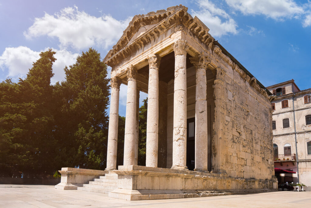 The Temple of Augustus in Pula, seen from below with its tall stone columns against a blue sky.