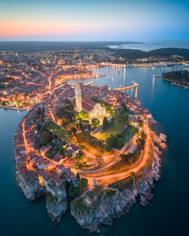 Aerial view of Rovinj old town and harbour at dusk, with St Euphemia's church tower above the peninsula.