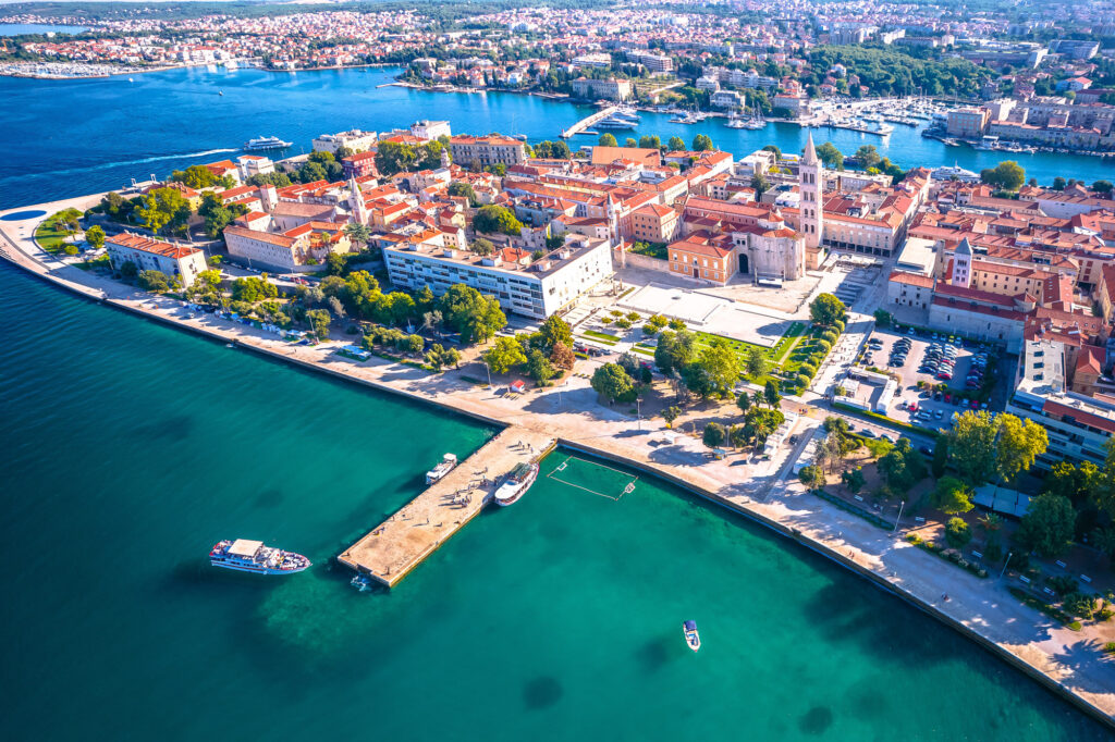 Aerial view of Zadar's old town peninsula, harbour and waterfront in bright sunlight.