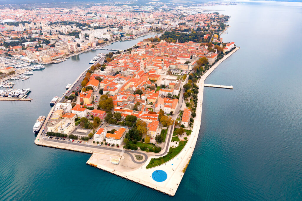 Aerial view of Zadar Old Town on its peninsula, with red-roofed buildings, harbour and Adriatic Sea.
