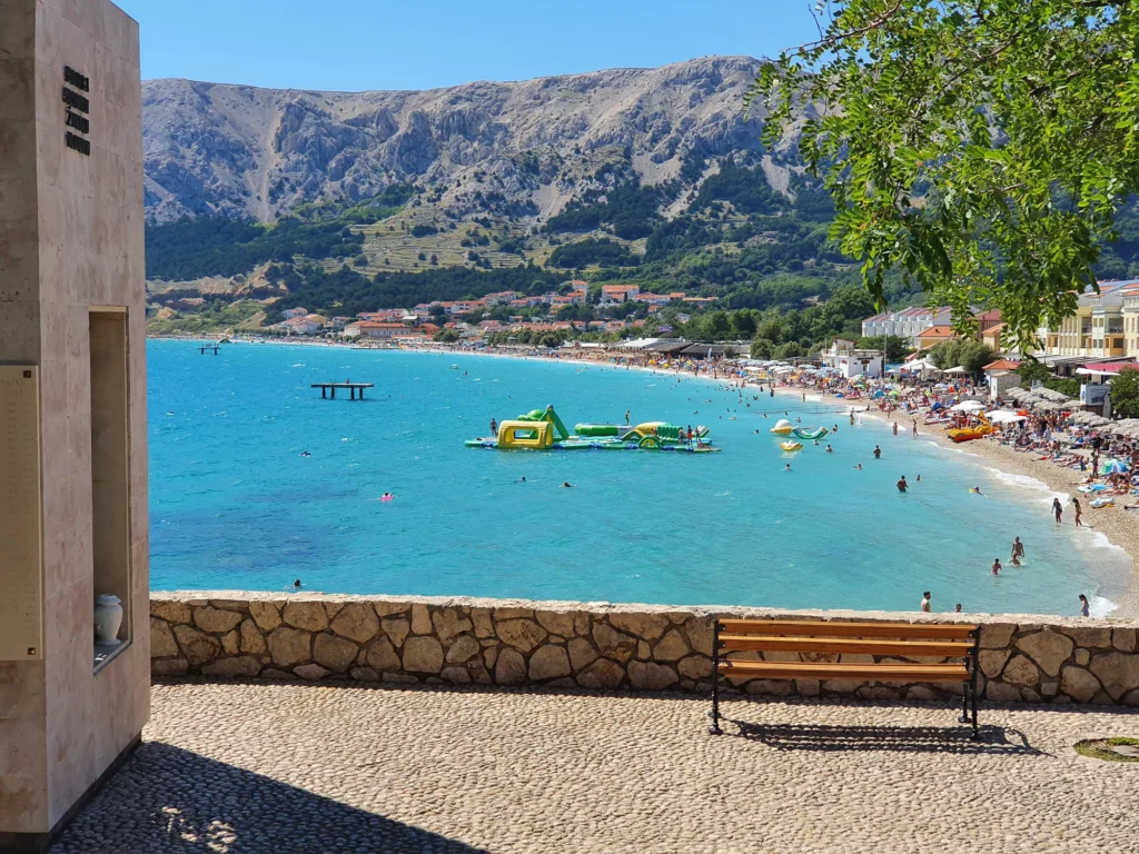 Vela Plaža in Baška, with swimmers, an inflatable water park and rocky mountains behind the beach