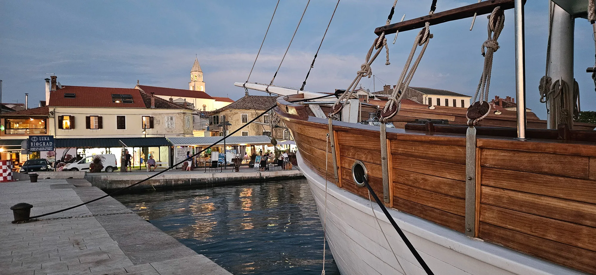 A wooden sailing boat moored beside the waterfront in Biograd na Moru at dusk.