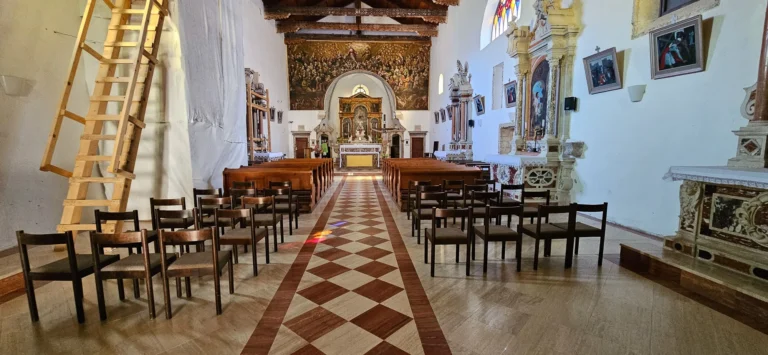 Church interior with rows of wooden pews, an ornate altar and a checkerboard-patterned aisle