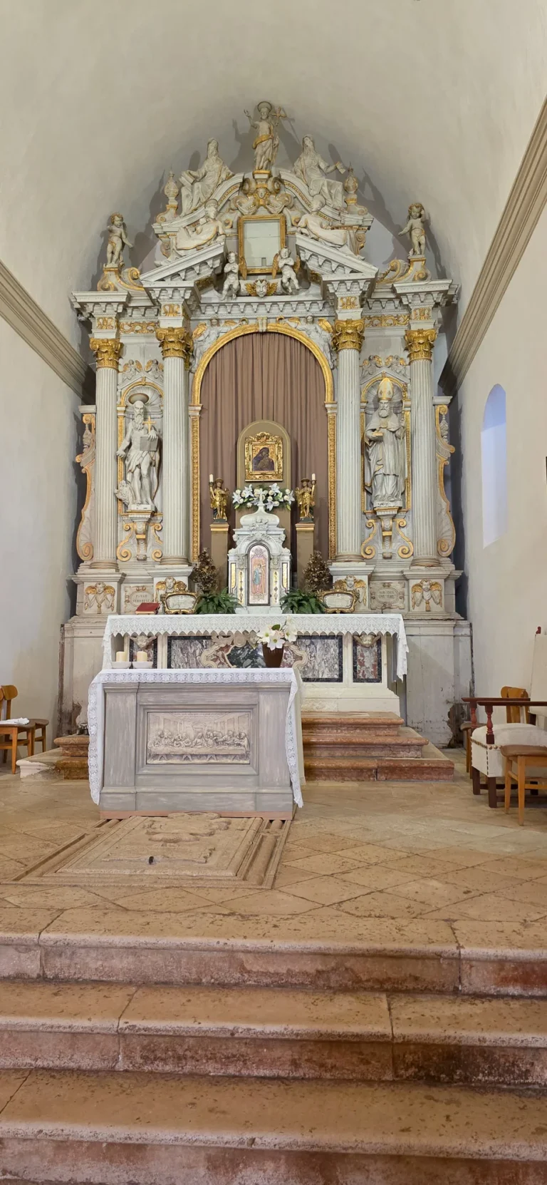 An ornate white-and-gold church altar with statues, flowers and a lace-covered altar table