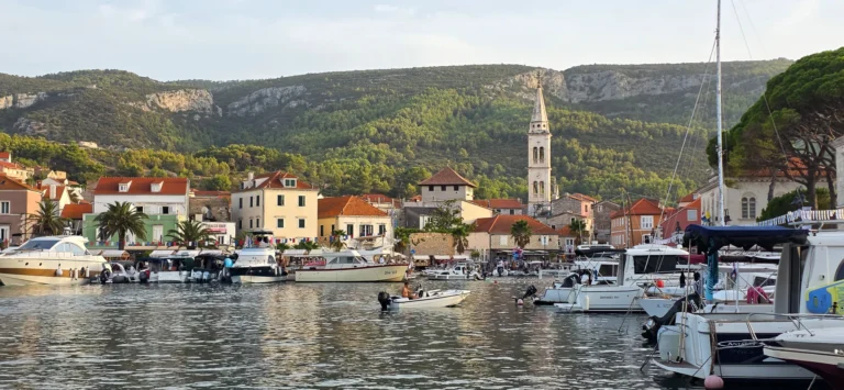 Boats fill a Croatian harbour in front of red-roofed waterfront buildings and a wooded hillside.