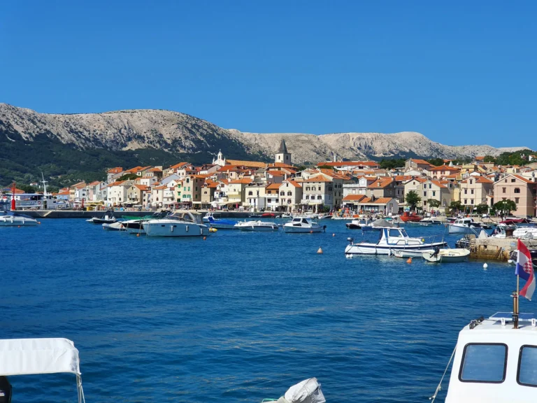 Boats in a Croatian harbour with a waterfront town and rocky mountains beyond