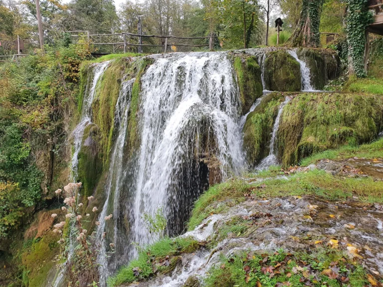 A wide waterfall spills over moss-covered rock in a wooded inland setting in Croatia.