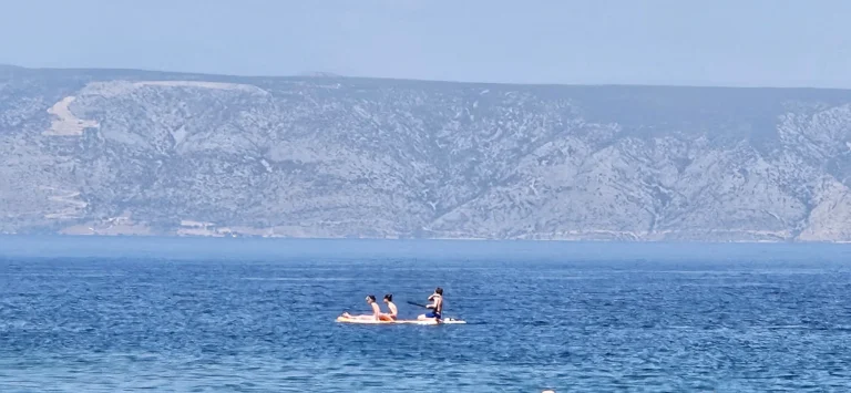 People paddleboarding on the blue sea with a rugged mountain coast in Croatia.
