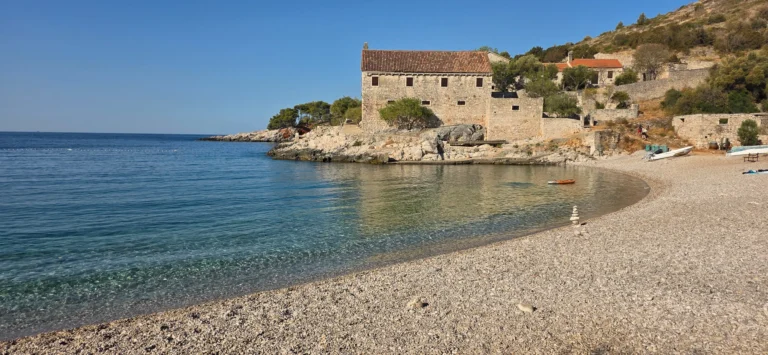 A pebble beach and clear cove beside a stone house on the Croatian coast