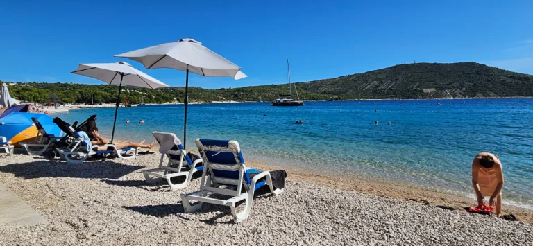 Pebble beach in Croatia with sun umbrellas, loungers and clear blue water in a sheltered bay