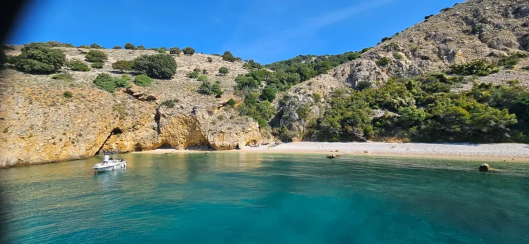 A small boat floats beside a pebble beach and rocky cove in Croatia.