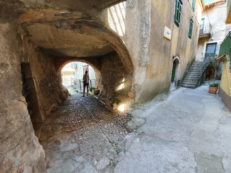 A cobbled stone alley passes beneath a low arch beside old buildings in Croatia.