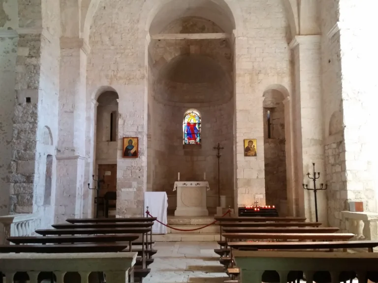 Stone church interior with wooden pews, an altar and a small stained-glass window