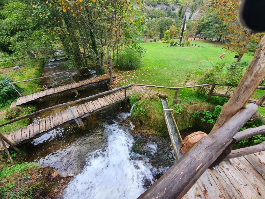 A stream cascades beneath wooden footbridges in a leafy inland setting in Croatia.