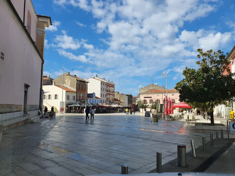 A paved town square in Croatia lined with colourful buildings, café terraces and outdoor seating.