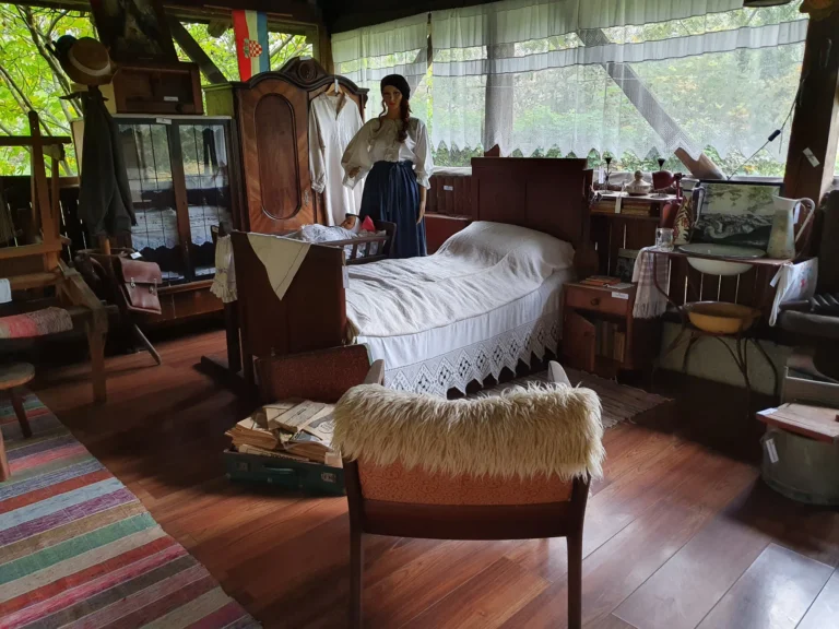 A traditional-style bedroom display with an antique wooden bed, furniture and a mannequin in folk clothing.