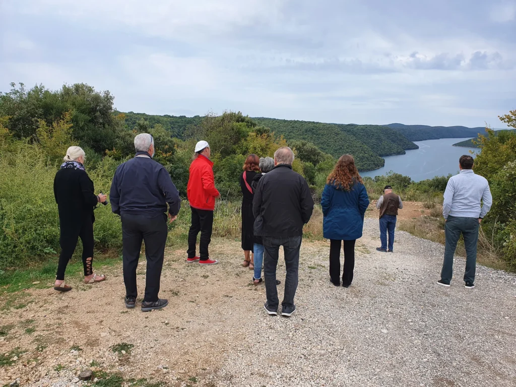 Visitors look across a wooded inlet from a gravel viewpoint in Croatia.