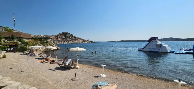 Pebble beach on the Croatian coast with sun loungers and a floating inflatable water park.