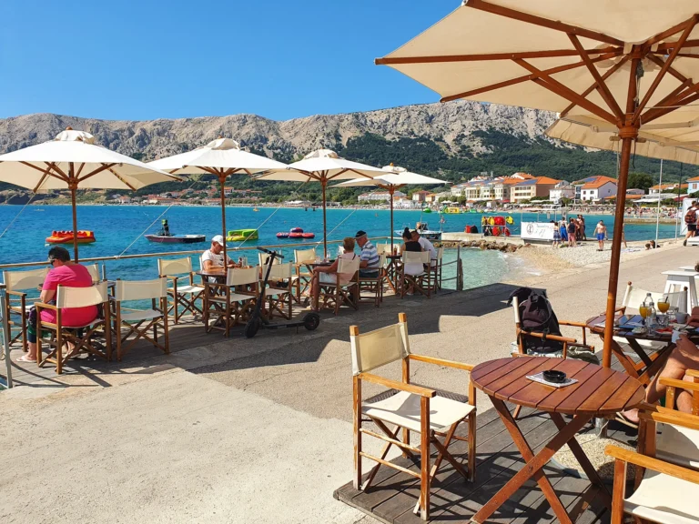 Seaside café terrace with umbrellas and tables overlooking a busy beach and blue water on the Croatian coast