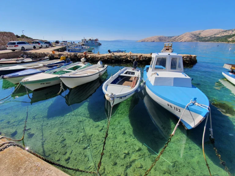 Small boats tied beside a stone harbour wall in clear turquoise water on the Croatian coast
