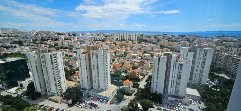 High-rise apartment buildings and dense city blocks overlook the sea beneath a partly cloudy sky.