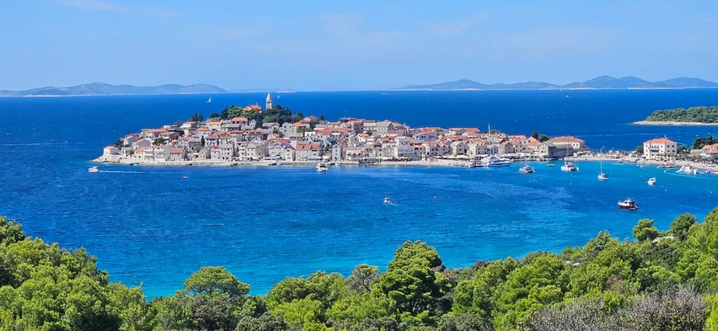 A Croatian coastal town with red-tiled roofs sits beside a deep blue sea dotted with boats.