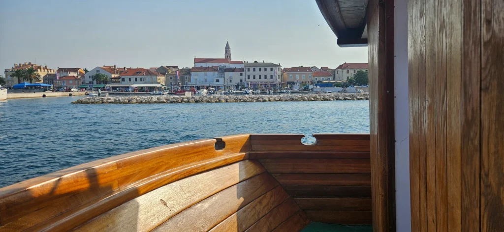 A wooden boat frames a Croatian harbour town across calm blue water.