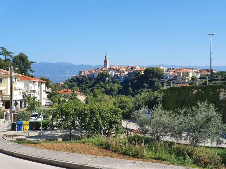 Hilltop town with a tall stone bell tower, red roofs and mountains in the distance