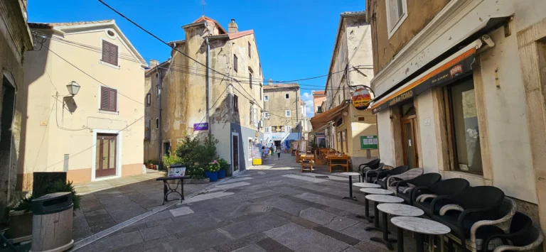 Stone-paved street lined with old buildings, outdoor café seating and a few pedestrians in Croatia