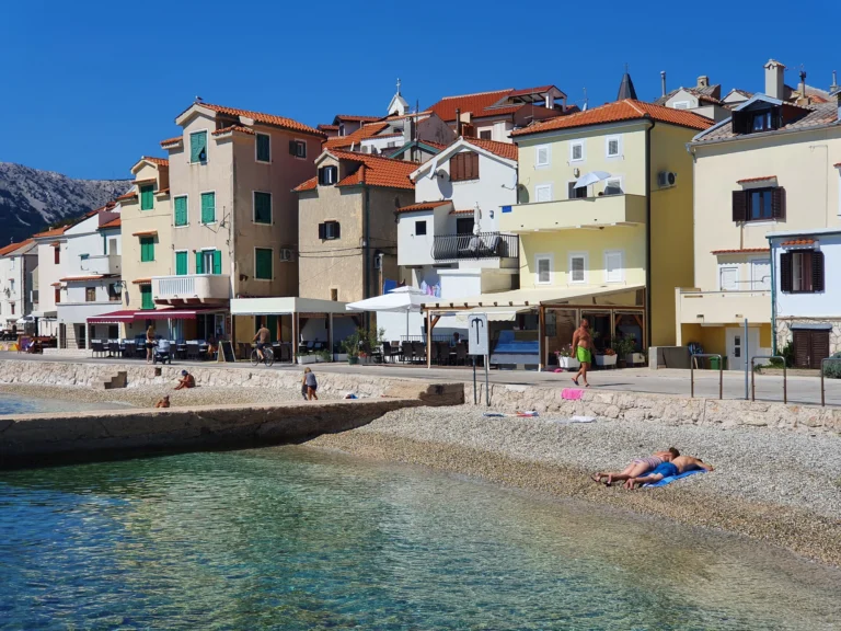 Small pebble beach and clear water below colourful waterfront houses on the Croatian coast