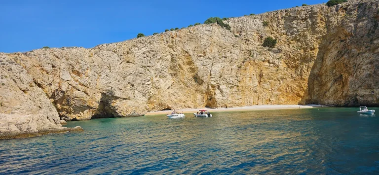 Small boats float beneath pale rocky cliffs along a sheltered Croatian cove.