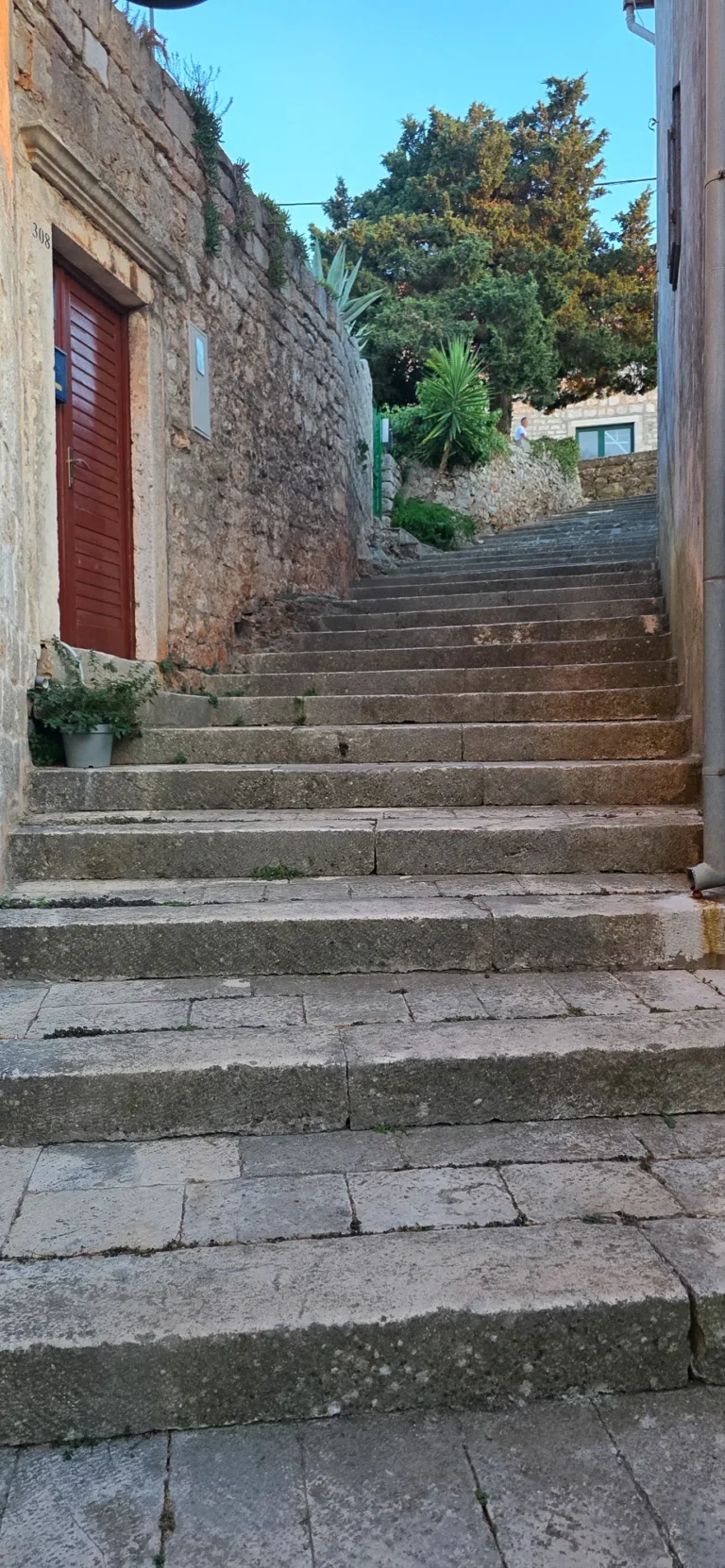 Worn stone steps climb through a narrow alley between rough stone walls and old buildings.