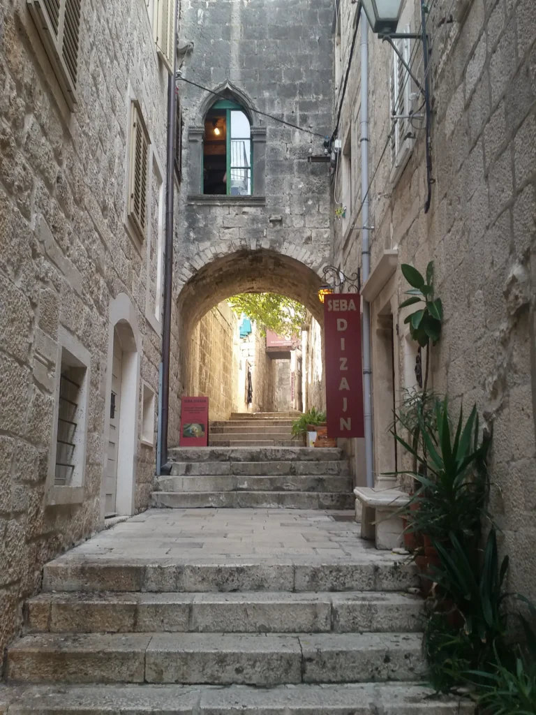 Stone steps lead through a narrow old-town alley beneath a stone arch.