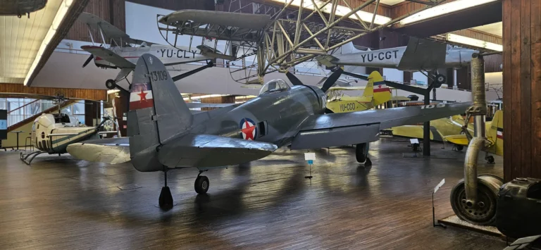 Several historic aircraft, including a dark fighter plane, displayed inside a museum hangar