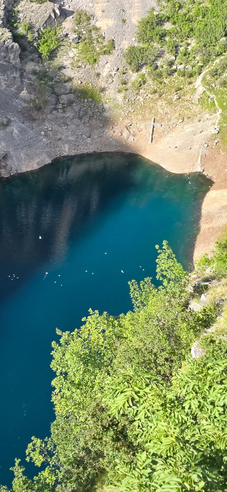 Turquoise water in a rocky karst basin at Blue Lake near Imotski, framed by green trees.