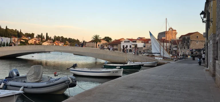 Boats moored beside the bridge and stone waterfront buildings in Jelsa harbour at sunset.