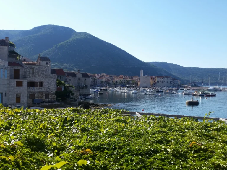 Boats moored in Komiža harbour, with stone buildings and a green mountain behind