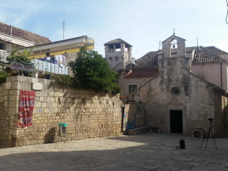 A small stone church and bell gable beside a paved square in Korčula Old Town.