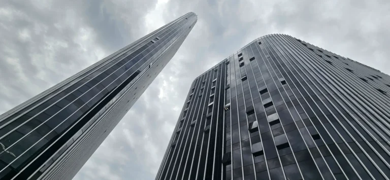 Two glass-clad skyscrapers viewed from below against a cloudy sky