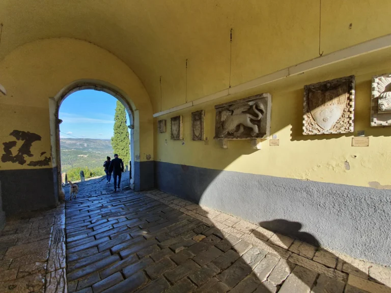 Stone reliefs line a passageway in Motovun's old town, with an archway opening onto the Istrian countryside.