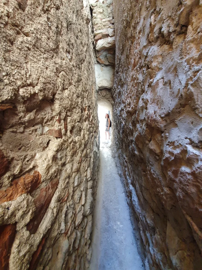 A person stands at the far end of a narrow passage between rough stone walls.