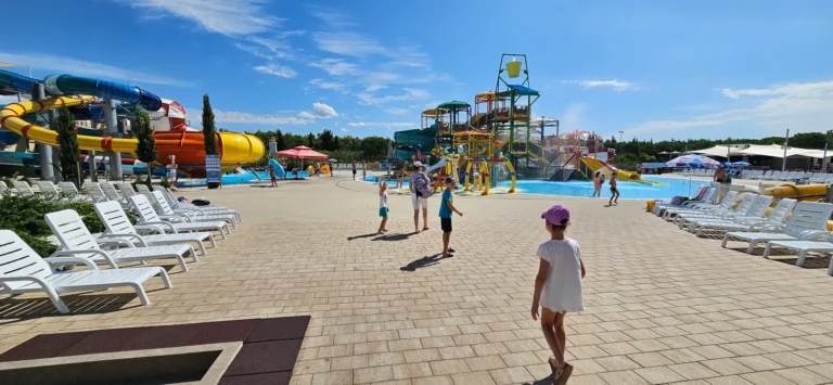 An outdoor water park with colourful slides, pools, rows of loungers and visitors on a sunny day.