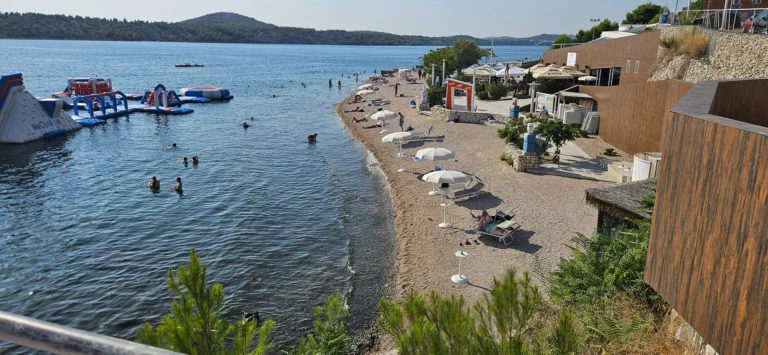 Pebble beach with a floating inflatable water park, swimmers and white umbrellas along the Croatian coast