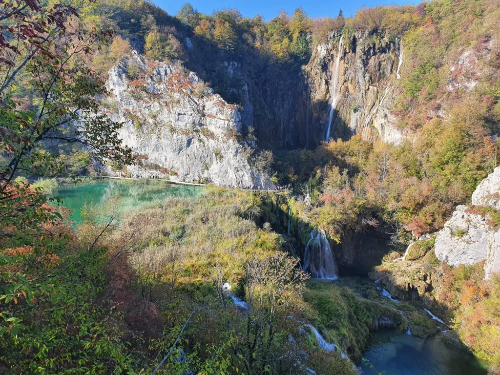 Waterfalls spill down limestone cliffs into a turquoise pool at Plitvice Lakes National Park in autumn.