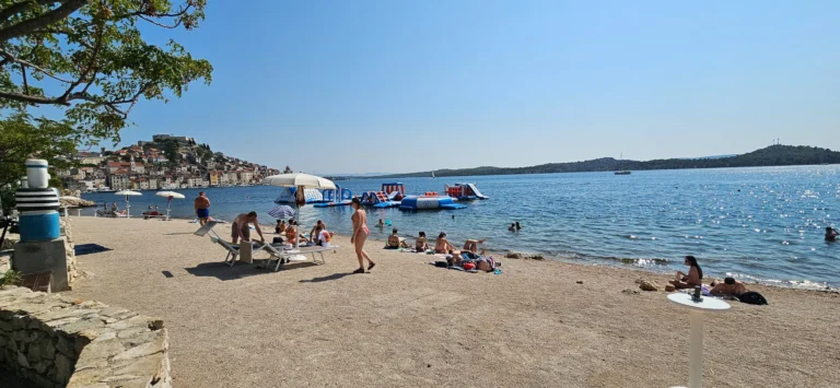 Swimmers and a floating water park at Raduča Beach, with Primošten's old town across the bay