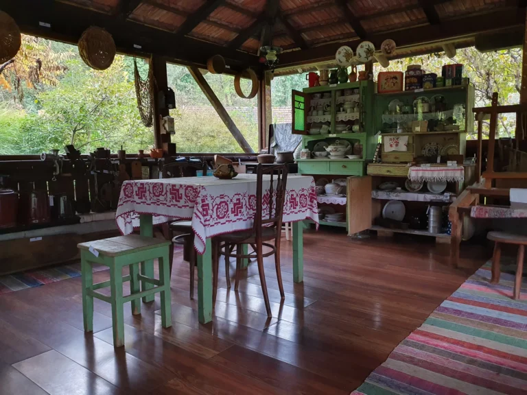 Rustic wooden interior with a green display cabinet, antique dishes and a table covered in a red-and-white cloth