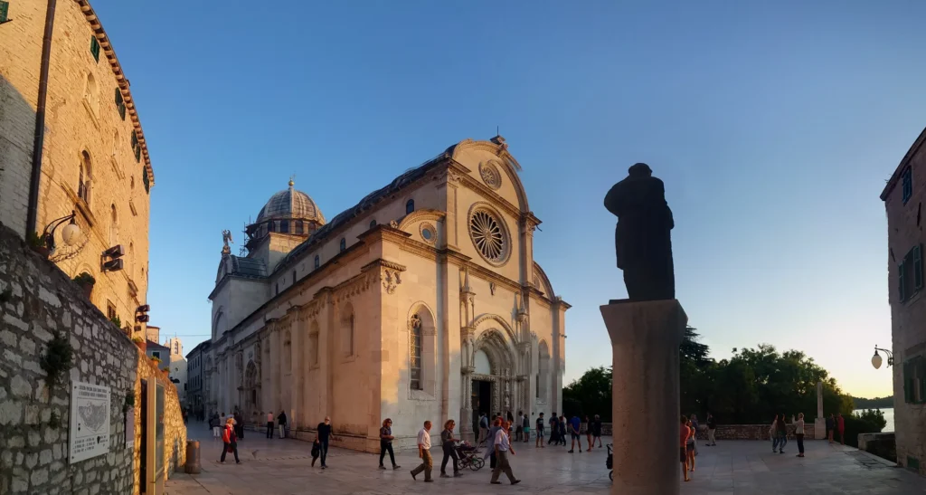 Cathedral of St James in Šibenik glows in evening light beside a silhouetted statue in the square.