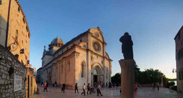 Cathedral of St James in Šibenik glows in evening light beside a silhouetted statue in the square.