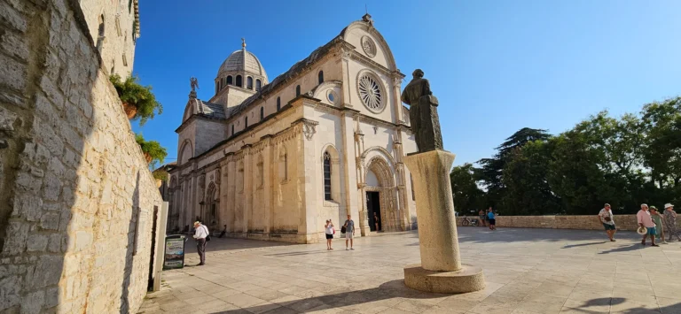 Cathedral of St James in Šibenik rises above a sunlit stone square, with a statue in the foreground.